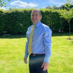 David standing outside on the grass with trees and a hedge in the background